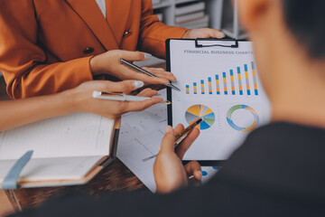 Asian businessman and woman working on laptop with digital tablet and analytical price charts at office desk, Business financial and accounting analytical concept.