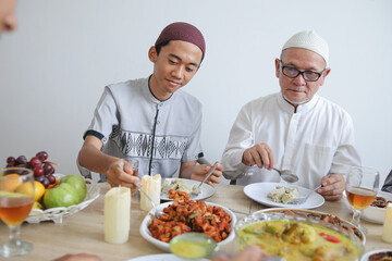 Portrait Of Young Asian Muslim Man Taking Food Together With His Grandfather on Celebrating Eid Al Fitr
