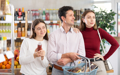 While shopping, man and woman couple with daughter walks through grocery store, studies windows, looks at assortment of snack, looking for something, seek products for promotions and discount prices