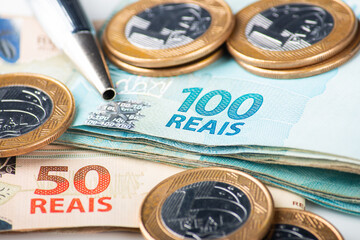 Close-up shot of Brazilian Real banknotes and coins with a pen, illustrating finance, economy, or business concepts in Brazil