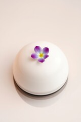 Elegant dessert: White dome topped with a delicate purple and yellow flower, minimalist design, and refined taste.