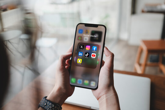 Bangkok, Thailand. February 28, 2025; Person holding a smartphone displaying a social media folder with apps including X, Instagram, Facebook, LinkedIn, TikTok, YouTube Snapchat in a cafe setting.