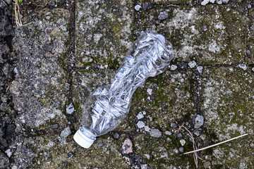 Top view of crumpled or crushed disposable plastic bottle on the ground. 