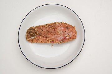 Person sprinkles seasoning and marinating chicken meat on a plate.