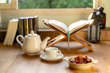 Many Date Palms are on bowls, plates, a cup of water, and the Quran, islamic style lamps on wooden tables, to wait for the time of Iftar, with the concept of ramadan Muslims around the world.
