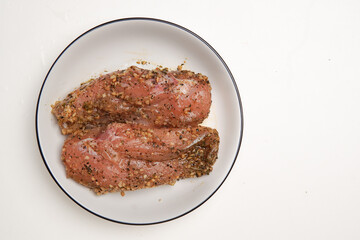 Marinated chicken meat covered in spices and sauce. prepared on top of a plate ready to be cooked.