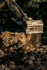 New house construction site earthworks, excavator moving dirt and piling it up, sunny winter day work site preparation, housing growth and development
