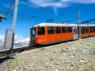Obraz premium Red tourist train on Gornergrat railway near Matterhorn peak on blue sky background on sunny day, summer season in Swiss Alps, tourist destination in Zermatt, Switzerland.