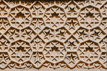 A detailed close-up of Islamic geometric patterns carved into a sandstone wall. 