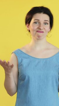 Vertical video. So-so gesture. Skeptical expression. Woman not sure dont know signaling uncertainty double feeling with hand movement facial expression isolated on yellow free space background.