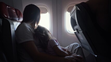 Young mother plays with little daughter in cabin of airplane