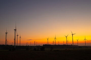 Wind turbines harnessing wind power during sunrise, set in an expansive agricultural landscape.