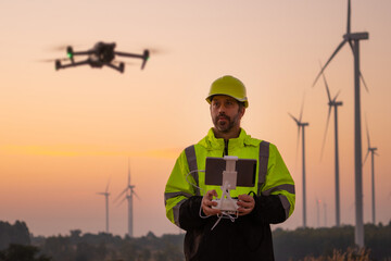 Engineers male flying drone surveying and checking wind turbines from the high angle view of the field during beautiful sunset. using drone technology for work.