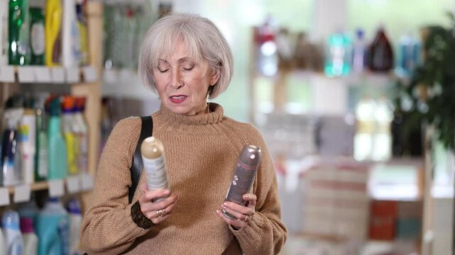 Elderly woman with gray hair choosing aerosol deodorant in household store. High quality 4k footage