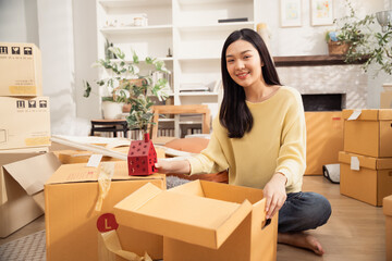 Fototapeta premium Asian smiling woman with packing cardboard boxes for moving to the new home. Concept of people moving house, buying property and decorating room