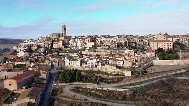 Shot of province Cervera, ancient European city located on hilly area in Segarra area. Dron aerial view of small compact city, winding city wall, twisted road- mountain serpentine