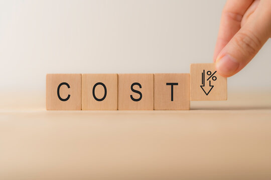 Cost reduction, business improvement and efficiency concept. Wooden block with word "COST" and a percentage and downward arrow icon, representing cost reduction, financial savings and efficiency.