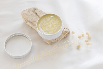 A delicate top-view arrangement featuring a spa balm placed on a natural stone, with a soft white satin fabric background for a luxurious and calming effect.