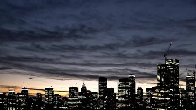 A time lapse of a city skyline captures skyscrapers as they shift from shadow to light, showcasing the sun rising and casting vibrant hues across the sky. For intro, transitions, or mood setting

