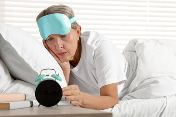 Overslept woman looking at alarm clock in bed indoors