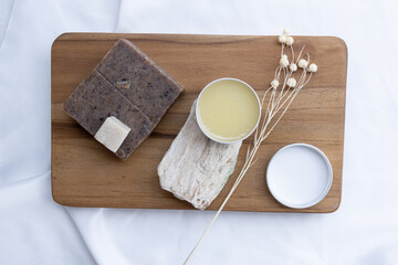 A contemporary beauty display where a spa balm rests on a textured stone, enveloped in the soft elegance of white satin for a high-end spa aesthetic.

