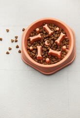 Dry pet food is in a slow feeder bowl on a tiled floor
