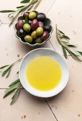 Olive oil and olives with olive branches resting on a tiled surface