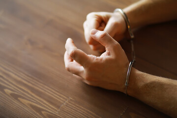 Close-up of Hands in Handcuffs on Wooden Table - Concept of Law Enforcement and Justice