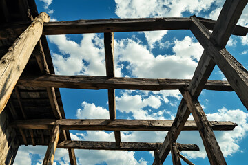 Obraz premium A house being built with wooden beams against a blue sky with clouds.