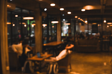 Blurry image of a cafe full of table and chair with dim lighting.