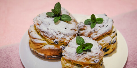 Eye-level shot of powdered sugar-dusted cruffins garnished with fresh mint on a white plate.