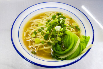 Fresh noodle soup with chopped green onion and salad leaf and aromatic broth in white blue bowl on table, Chinese traditional food, close-up.