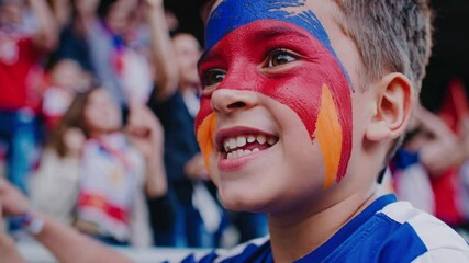 Excited Armenian child with face painted in Armenia flag colors, joyful patriotic expression, national pride at stadium  
