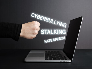 Fist hitting laptop screen with cyberbullying, stalking and hate speech texts