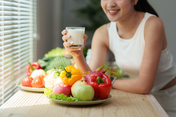 Woman holding glass of milk with fresh fruits and vegetables on table