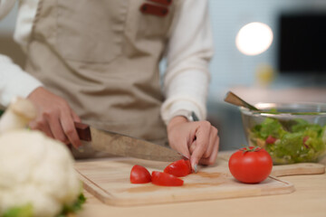 Chef slicing tomatoes on cutting board, preparing ingredients for fresh salad in restaurant kitchen