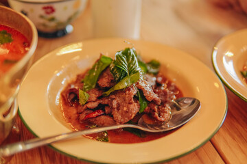 Stir-fried holy basil beef slices with vegetables on a white plate, restaurant setting.