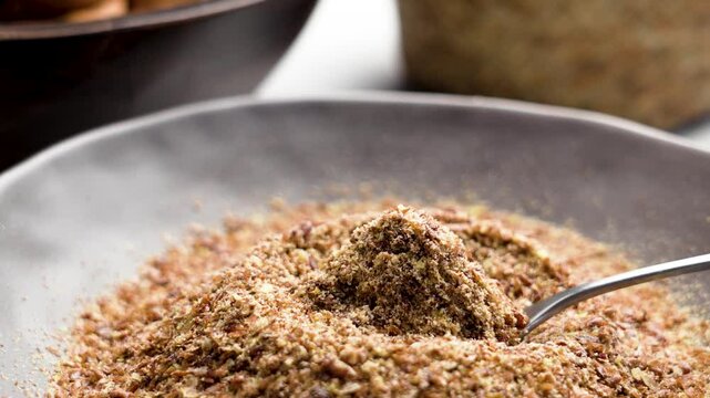 Full bowl of ground flaxseed with metal spoon on kitchen table close up. Organic nutritious ingredient