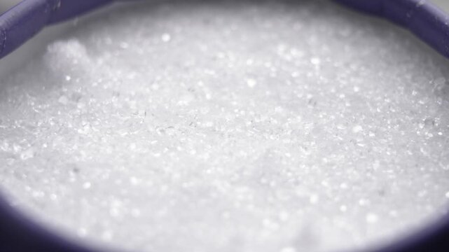 Epsom salt crystals falling into blue cardboard container in slow motion close up. Skincare spa ingredient