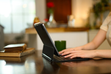 Close up shot of a woman hands typing on digital tablet with keyboard on a wooden dining table