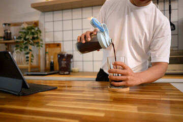 Man pouring mixed chocolate protein shake from a shaker bottle into a glass in a modern kitchen