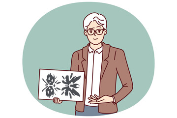 Man psychotherapist holds picture of rorschach test to determine patient personality type. Elderly psychotherapist demonstrates piece of paper with blots for medical psychiatric experiment.