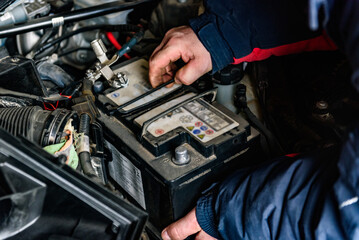 A mechanic removing an old car battery from the box. Car repair.