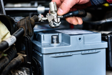 A man installing a new car battery under the hood of a car. Vehicle maintenance and repair.