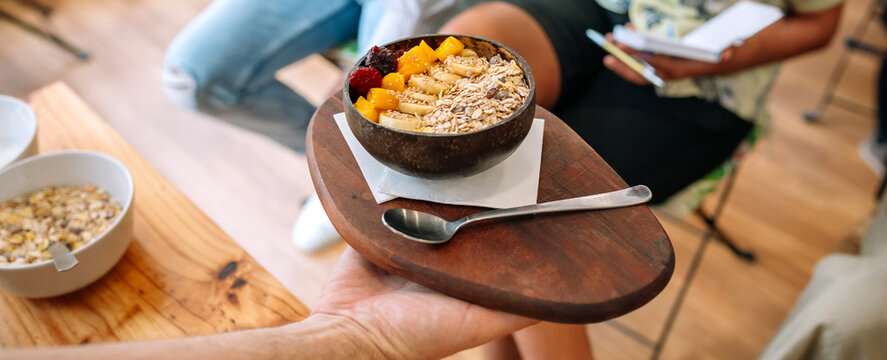 Banner of unrecognizable chef showing vegan breakfast bowl made with mango, banana, raspberries, cereals and muesli to bloggers and influencers taking pictures with smartphones in cooking master class