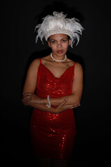 Low key portrait of young curly woman in red dress with headdress made of bird feathers