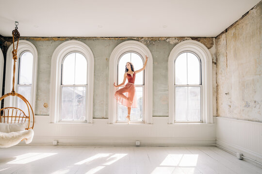 Ballerina en pointe poses in an arched window of a rustic loft