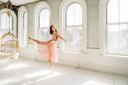 Ballerina performs an arabesque en pointe in a sunlit vintage studio