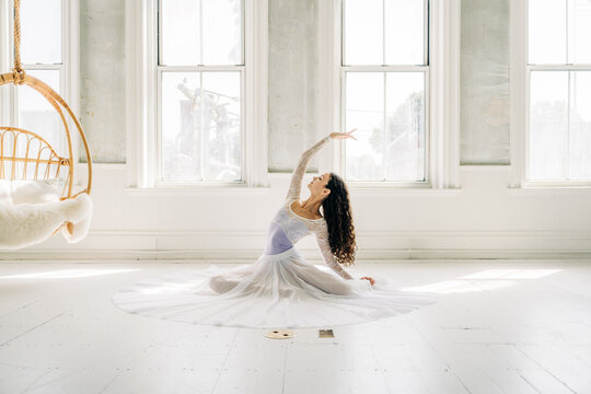 Ballerina gracefully stretches on the floor, reaching upward