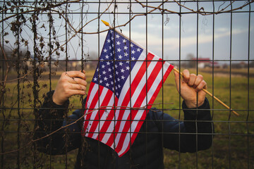 Concept of United States of America closed borders. Sad man at barbed fence., holding USA flag